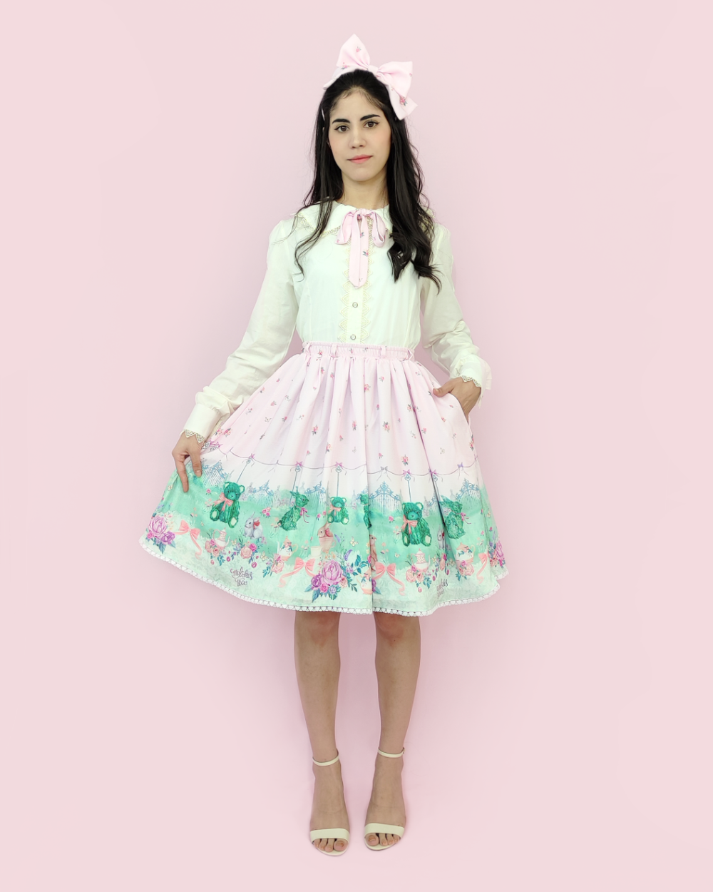 Model wearing skirt made of pink polyester printed with a garden full of bunnies, teddy bears, cups and teapots, flowers and a beautiful lawn.