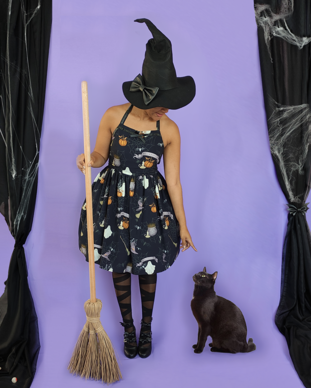 Witch wearing Halloween sleeveless dress in black and holding a broomstick with her cat